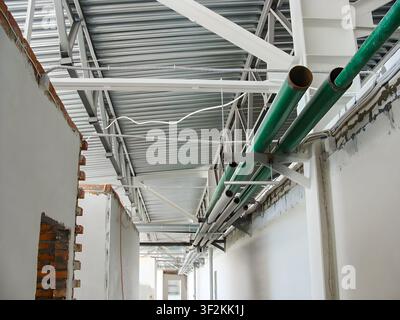 Cantiere edile con tubi verdi esposti e soffitto in metallo ondulato con muratura incompiuta e pareti bianche Foto Stock