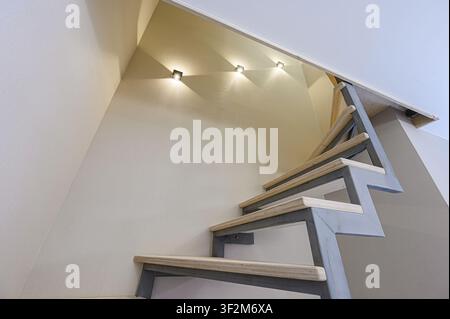 Scatto ad angolazione bassa di una moderna scala in legno contro un muro beige con tre piccole luci. Design minimalista Foto Stock