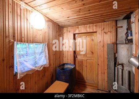 stanza sauna rustica con pareti, soffitto e porta in legno. Contiene una botte blu, una panca e una finestra coperta da una tenda Foto Stock