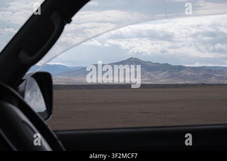 Vista dal finestrino di un'auto di un paesaggio desertico arido con montagne sotto un cielo nuvoloso. Immagine di sfondo multiuso adatta per viaggi, viaggi su strada, a Foto Stock