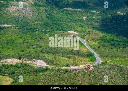 Strada tortuosa si snoda attraverso colline verdi e rigogliose sotto un cielo blu brillante Foto Stock