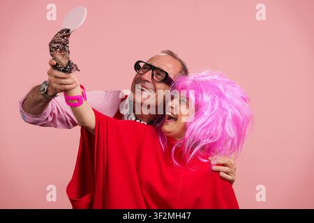 Coppia matura che si diverte con una parrucca rosa e uno specchio Foto Stock
