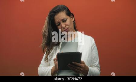 Donna che tiene il tablet con la mano sulla testa e che sgombra in studio mentre legge e tocca il touchscreen; frustrazione. Foto Stock