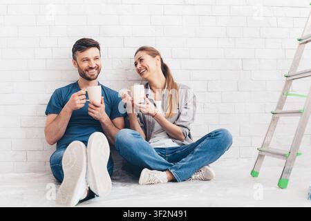 Giovane coppia sorridente bere tè e caffè in appartamento nuovo Foto Stock