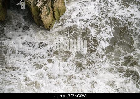 Onde schiumose si infrangono contro le scogliere di gesso della riserva naturale di Bempton Cliffs, East Yorkshire, viste dall'alto. Foto Stock