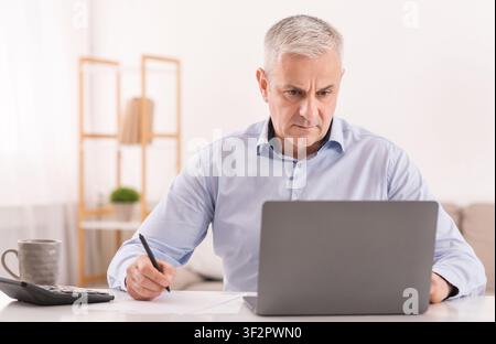 Uomo anziano che usa il laptop in ufficio e scrive le note Foto Stock