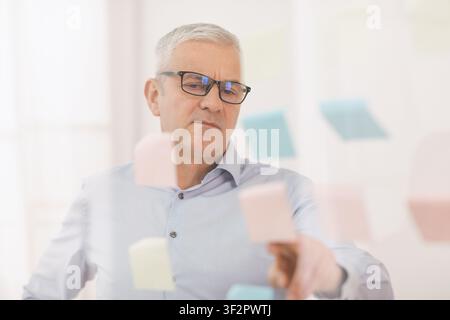 Responsabile anziani che mette le note adesive sulla finestra Foto Stock