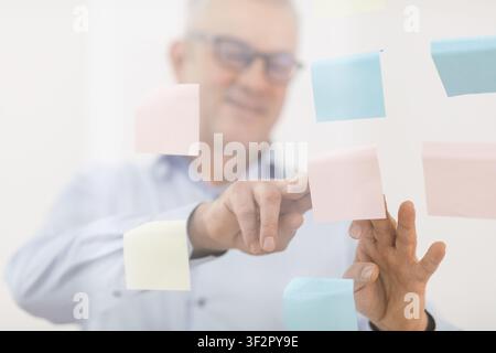 Responsabile anziani che mette le note adesive sulla finestra Foto Stock