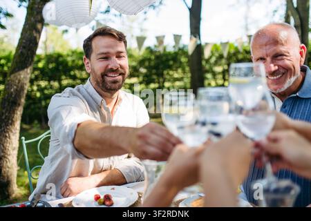 Brindisi multigenerazionali in famiglia durante una festa al barbecue all'aperto. Foto Stock