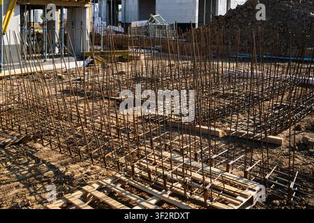 Rete di acciaio di rinforzo disposta sistematicamente su una fondazione di cantiere edile. Il terreno è preparato con supporti in legno e elementi strutturali circostanti visibili sullo sfondo. Foto Stock