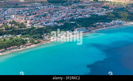 Kallithea, Grecia, 9 luglio 2026. Una veduta aerea mostra una città costiera lungo una brillante costa turchese con una lunga spiaggia sabbiosa e edifici strettamente accatastati Foto Stock
