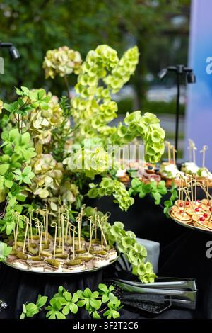 Un elegante tavolo da banchetto per catering decorato con fiori verdi rigogliosi e servito con vari antipasti gourmet, canapé e tartine all'aperto Foto Stock