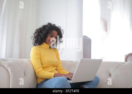 Donna nera felice seduta su un divano che usa un laptop Foto Stock
