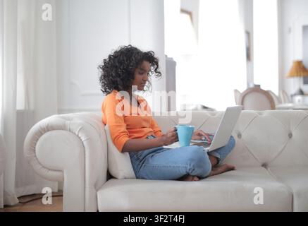 Giovane donna nera lavora su un laptop a casa Foto Stock