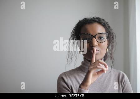 Donna nera con un dito sulle labbra che chiede silenzio Foto Stock