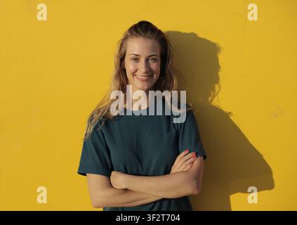 Giovane donna felice che sorride davanti a un muro giallo brillante Foto Stock