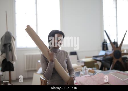 Giovane donna sorridente che tiene un rotolo di carta in uno studio d'arte Foto Stock