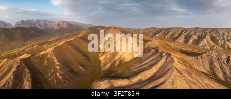 Vista aerea del paesaggio montano aspro vicino a Kol-Suu, con dolci colline dorate, picchi rocciosi drammatici e un vasto cielo nel distretto di At-Bashi Foto Stock