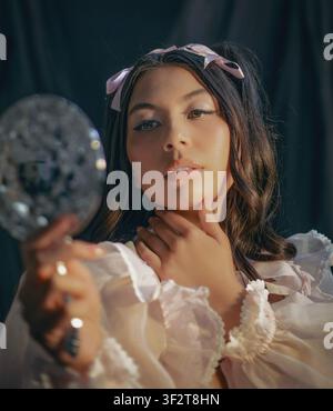 Giovane donna eterea guarda in uno specchio scintillante Foto Stock