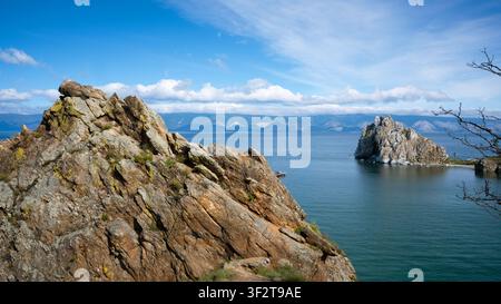 Una fotografia paesaggistica con una grande formazione rocciosa strutturata in primo piano, ricoperta da macchie di licheni gialli e vegetazione verde rada Foto Stock