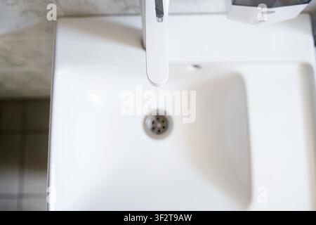 Vista dall'alto di un moderno lavandino in ceramica bianca con un rubinetto elegante, dettaglio di scarico pulito ed elementi di design interno minimalisti in un bagno di casa Foto Stock