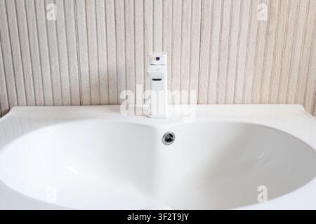 Vista ravvicinata frontale di un lavandino in ceramica bianca vuoto con un moderno rubinetto miscelatore bianco e uno scarico cromato su pannelli di legno chiaro in un Foto Stock