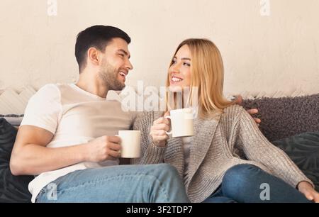 Una coppia felice con bevande calde che si rilassano sul divano a casa Foto Stock