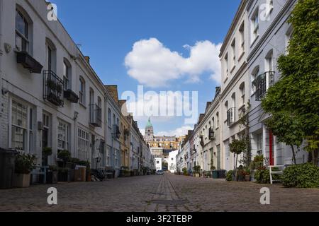 Storiche case residenziali fiancheggiano la strada acciottolata di Kensington, Londra, con una torre di chiesa visibile in lontananza. Londra, Regno Unito, 24 maggio 2023 Foto Stock