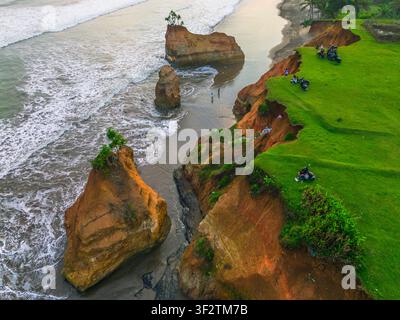 Vista aerea delle drammatiche scogliere costiere e degli scogli marini al tramonto, con erba verde rigogliosa sul bordo della scogliera e onde che si infrangono contro la riva a B Foto Stock