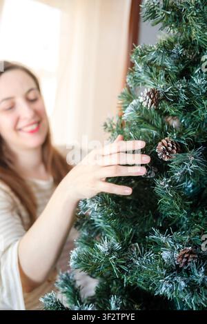 Donna sorridente, che sistema pigne su un albero di Natale ghiacciato Foto Stock