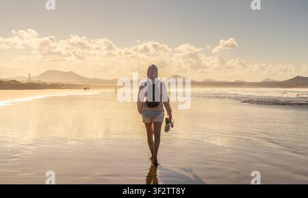 Viaggiatore solitario che esplora una vasta spiaggia scenografica durante l'ora dorata Foto Stock