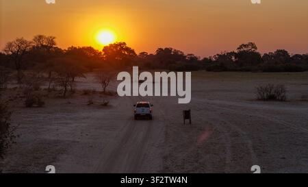 Vista aerea di un veicolo che percorre una strada sterrata attraverso il paesaggio della savana durante un vivido tramonto nel Delta dell'Okavango, Distretto Nord-Ovest, B Foto Stock