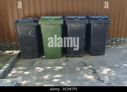 Grandi contenitori di spazzatura in plastica stanno con i coperchi chiusi sul marciapiede lastricato vicino alla recinzione. Foto Stock