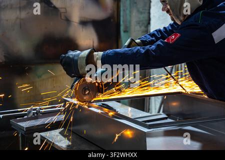 Lavoratore industriale che taglia il metallo con una smerigliatrice angolare in un'officina di produzione Foto Stock