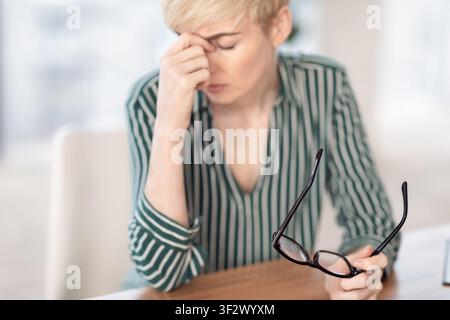 Businesswoman Matura Con Mal Di Testa Oculare Massaggiante Nosebridge Sul Posto Di Lavoro Foto Stock
