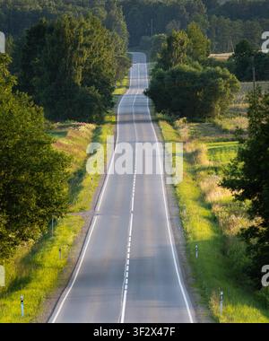 Una strada rurale vuota e ondulata che si estende attraverso la campagna estiva vicino a Viesīte, Lettonia. Foto Stock