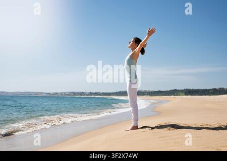 Donna in piedi su una spiaggia sabbiosa con le braccia sollevate verso il sole Foto Stock