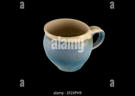 Tazza da caffè in ceramica blu fatta a mano con corpo arrotondato e manico robusto, fotografata su sfondo nero. Texture smaltata rustica e interno terroso Foto Stock