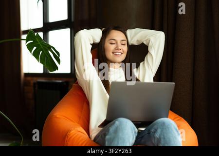 Sorridente bella donna sittingon su poltrona con computer portatile Foto Stock