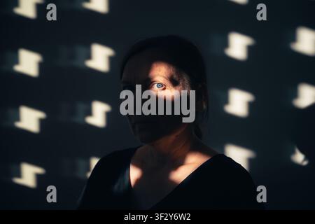 Ritratto di una donna parzialmente illuminata da luce solare e ombre a motivi. Messa a fuoco selettiva. Foto Stock