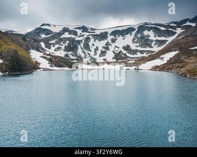 Lago glaciale di montagna circondato da picchi innevati e da un paesaggio aspro sotto un cielo nuvoloso Foto Stock