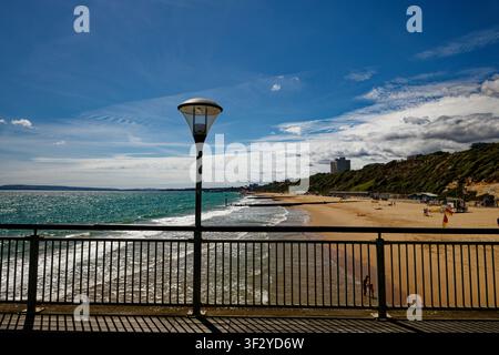 Una lanterna con ringhiere su un molo sopra una larga spiaggia sabbiosa con scogliere vegetate e un hotel sul lungomare, Boscombe Beach, Bournemouth, Dorset, Inghilterra. Foto Stock