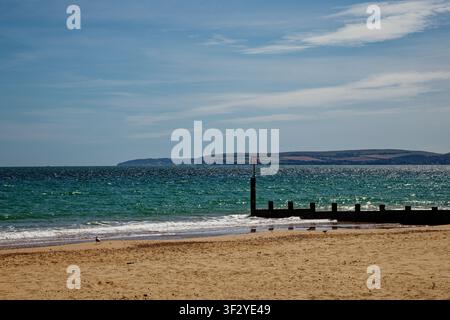 Morbide onde che lambiscono una spiaggia di sabbia dorata con una groyne e un promontorio lontano attraverso un mare blu-verde, Bournemouth, Dorset, Inghilterra. Foto Stock
