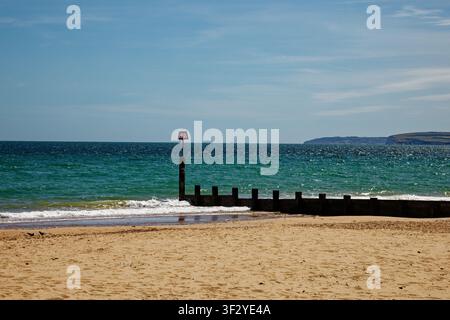 Morbide onde che lambiscono una spiaggia di sabbia dorata con una groyne e un promontorio lontano attraverso un mare blu-verde, Bournemouth, Dorset, Inghilterra. Foto Stock