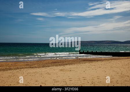 Morbide onde che lambiscono una spiaggia di sabbia dorata con una groyne e un promontorio lontano attraverso un mare blu-verde, Bournemouth, Dorset, Inghilterra. Foto Stock