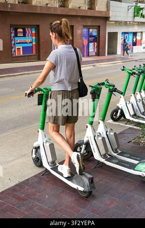 DALLAS, TX, USA - 11 LUGLIO 2026: Una persona è vista mentre interagisce con uno scooter Lime parcheggiato su un marciapiede in città. Gli scooter Lime sono veicoli elettrici popolari Foto Stock