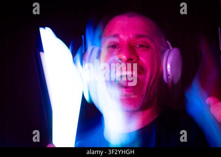 Uomo con cuffie che si muove ed esprime gioia nella luce neon colorata Foto Stock