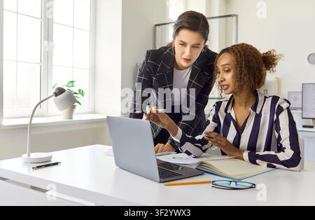 Due donne d'affari che collaborano su un laptop in un ufficio moderno, pianificando una strategia Foto Stock