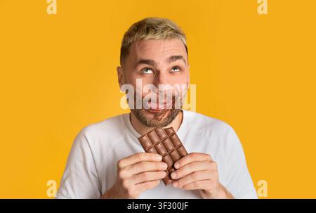 Divertente ragazzo mangia cioccolato e rotola gli occhi Foto Stock