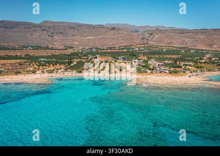 Veduta aerea della spiaggia di Xerokambos con acqua turchese limpida, un piccolo villaggio costiero e campi agricoli sullo sfondo di montagne aride nel sud-est di C Foto Stock